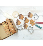 Photo d'un plan de travail de cuisine ou est posé des biscuits de noël décoré à l'aide des stylos et des emportes pièces disposés sur la table. une partie des gâteaux sont rangés dans une boite en carton craft 