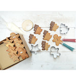Photo d'un plan de travail de cuisine ou est posé des biscuits de noël décoré à l'aide des stylos et des emportes pièces disposés sur la table. une partie des gâteaux sont rangés dans une boite en carton craft 