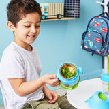 jeune garcons qui souris et tient dans sa main droite une boite à repas avec des poignées bleus, sa boite contient des pates et des légumes