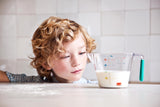 Photo d'un petit garçon qui regarde un bol mesureur avec du lait a l'intérieur