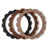 Ensemble de 3 bracelets en silicone, posés les uns devant les autres. ils sont en forme de fleurs et ont 3 couleurs différentes :  noir, marron et beige