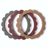 Ensemble de 3 bracelets en silicone, posés les uns devant les autres. ils sont en forme de fleurs et ont 3 couleurs différentes : sauge, bordeaux et marron