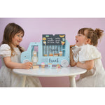 Photo de 2 jeunes filles qui sont assisent autour d'une table et jouent avec un jeu qui represente un food truck avec son cuisinier et ses ingrédients