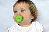 Photo d'un bébé au yeux bleu qui tiet dans sa bouche une tétine avec une forme de trèfle