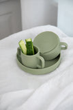 Assiette en silicone de couleur vert olive avec posé dedans une tasse en silicone avec anses de la même couleur et un bol posé à l'envers