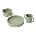 Vaisselle en silicone pour enfant sur un fond blanc, il y 3 objets une assiette, un bol et une tasse à anses. La vaisselle est de couleur vert olive