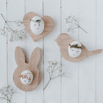 3 œufs avec des visages dessinés dessus et des brindilles de fleurs séchées qui remplace leur cheveux. Les oeufs sont disposé dans des coquetiers en bois en forme de lapin, coeur et oiseau