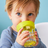 Photo d'un jeune garçon aux yeux bleu qui boit dans un verre en verre avec un embout de couelur vert