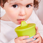 Gros plan sur un enfant qui boit dans une tasse verte et bleu