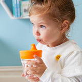 Petite fille entrain de boire dans un verre doté d'un couvercle avec un bec verseur de couleur orange