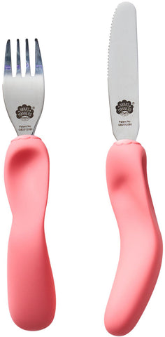  Une fourchette et un couteau aux manches ergonomiques de couleur rose, posé les un a coté des autres. Les couverts sont en inox avec la marque gravé sur le dessus, il s’agit de la marque Nana’s Manners représenté par une tête de mamie