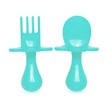 Couverts ergonomique pour enfants turquoise. Il y a une fourchette et une cuillère, elles sont sur un fond blanc. Le manche est ergonomique et petit, il y a une collerette en forme de fleur sur chaque couverts