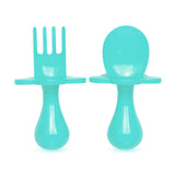 Couverts ergonomique pour enfants turquoise. Il y a une fourchette et une cuillère, elles sont sur un fond blanc. Le manche est ergonomique et petit, il y a une collerette en forme de fleur sur chaque couverts