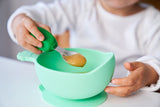 Gros plan sur une petite cuillère rempli de compote, tenue dans la main d'un enfant. La cuillère à une manche arrondi de couleur vert?