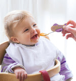 Bébé assit sur une chaise haut souriant et entrain de manger avec une petite cuillère en forme d'avion