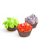 3 cupcake avec glaçage de couleurs vert, rouge et violet. Sur le glaçage il y a des yeux. Les gâteaux sont posés sur un fond blanc