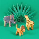 Photo de 3 biscuits en forme d'élephant, girafe et lion. Ils sont posés sur un fond vert avec un origami dans le fond. Les biscuits sont en 3D et décorés avec des couleurs