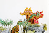3 biscuits sablés en forme de dinosaure en 3D, décorés avec glaçage de plusieurs couleurs. Les dinosaures en biscuits 3d décorés sont dans un décor de jungle artificielle: rocher, mousse et arbre.