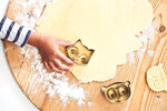 Photo prise par le haut d'un plan de travail de cuisine avec posé dessus de la pâte sablé avec lamain d'un enfant qui y pose un emporte pièce en acier en forme de renard