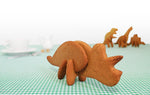 En avant plan TRiceratops en biscuits 3D et en arrière plan 3 autres dinosaures fait en biscuit. Les dinosaure sont sur une table dont la nape est en vichy vert