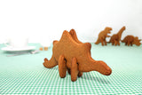 En avant plan Steposaure, dinosaure en biscuits 3D et en arrière plan 3 autres dinosaures fait en biscuit. Les dinosaure sont sur une table dont la nape est en vichy vert