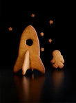Photo de plusieurs biscuits en forme de vaiseau spatiale, d'astronaute et d'etoile. La photo est prise sur un fond noir. Les biscuits sont en 3D
