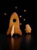 Photo de plusieurs biscuits en forme de vaiseau spatiale, d'astronaute et d'etoile. La photo est prise sur un fond noir. Les biscuits sont en 3D