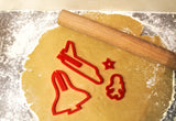 Photo prise du haut d'une table de cuisine avec étalé dessus, a l'aide d'un rouleau a patisser, une pâte a biscuit. Sur la pâte est disposé 4 emportes-pièces de couleurs rouge représentant une fusée et un astronaute