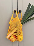 Filet à provision de couleur jaune accroché à une porte. Il contient des pommes et un poireau