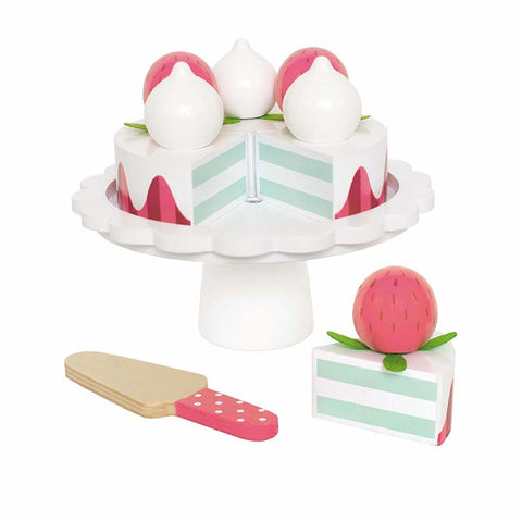 Jouet pour enfant en bois en forme de gâteau aux fraise. Le gâteau est posé sur un plateau de présentation blanc, il se coupe en 6 part et il dispose de fraise et de meringue sur le dessus. Devant le gâteau est posée une pelle à gâteau