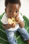 Photo d'un bebe qui est assit et regarde l'objectif en portant a sa bouche un jouet de entition en forme de tranche de pomme