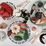 Photo d'une table d'enfant avec posé dessus de la vaisselle pour enfant avec des couverts et des assiette. Il ya des jouets de dentition aux formes de fruits et legumes mélangés à de vrais ingrédients