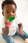 Photo d'un bébé assit par terre qui tient dans sa bouche un jouet de dentition en forme de radis