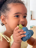 Phot d'une jeune fille souriante qui tient dans sa bouche un jouet en fore de grappe de myrtille.