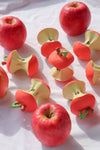 Plusieurs pommes rouges et trognons de pommes posés sur une nappe blanche. Les trognons sont des jouets de dentition qui ressemble fortement a des vrais fruits. Les pommes entières sont de vrais fruits