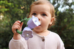 Photo d'un bébé qui tient dans sa main un jouet en forme de fleur blanche avec un anneau vert. les couleurs du jouets sont trés proches de la réalité. La photo est prise en mettant au centre la fleur