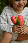 jeune fille souriante qui tient dans sa main des jouets en caoutchouc en forme de tulipe. La photo est prise avec un gros plan sur ses mains, avec le bouquet de tulipes dedans