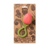 Jouet de dentition sur fond blanc, en forme de fleur. Il représente une tulipe, les couleurs et détails sont très proche de la réalité. La fleur est disposé dans son emballage de la marque Oli&Carol, il s'agit d'un simple carton de couleur craft aec des dessin de fleurs et des instructions sur le produits