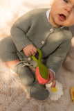 bébé habillé avec un ensemble en maill de couleur kaki et avec les chausson assortis. Il tient dans sa main un jouet en caoutchouc qui à la forme et la couleur d'une tulipe