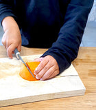 Main d'enfant qui coupe un abricot avec le couteau pour enfant kiddikutter de couleur gris