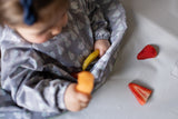 Gros plan sur les details d'un bavoir à manche longue de culeur grise avec des illustration de poires et pommes. L'enfant tient dans sa main des morceaux de fruits, pomme et fraise