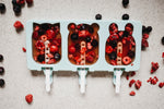 Photo d'un moule a glace en forme de 3 Animaux, contenant su sirop rouge avec des morceaux de fruits rouge a l'intérieur. Sur la table est posé un peu partout des brisures de fruits rouges
