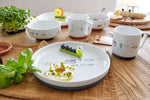 Photo d'une table à manger en bois avec posé dessus de al vaisselle pour enfant en porcelaine blanche avec des illustrations sur la nature dessus