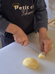 Photo des main d'un enfant qui coupe une pomme en petit morceau . L'enfant est habillé d'un tablier bleu avec des ecriture : petit chef Sohenn