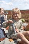 Photo de 2 jeunes filles qui pique-nique dans un champ. La jeune fille au premier plan tient dans sa main une gourde en ino avec un tracteur et celle de derrière boit dans une bouteille.