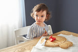LP Jeune fille qui regarde dans le vide, elle est assise devant une table et est entrain de manger des fraises coupé sur une planche en bois