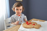 Jeune fille qui regarde dans le vide, elle est assise devant une table et est entrain de manger des fraises coupé sur une planche en bois