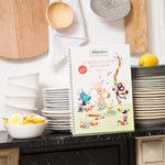 Plan de travail d'une cuisine avec de la vaisselle blanche empilées et un livre de recette pour enfants posé dessus.