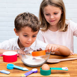 Photo de 2 enfants, un garçon et une fille qui sont entrain de cuisiner avec des tasses de mesure colorées
