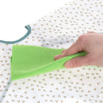 Gros plan d'un main d'adulte tenant une lavette de couleur verte et qui nettoie un tablier pour enfant